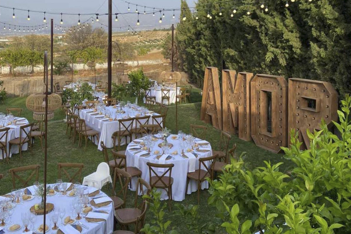 Mesas y sillas en modo banquete en el jardín junto a unas letras grandes que pone "AMOR"