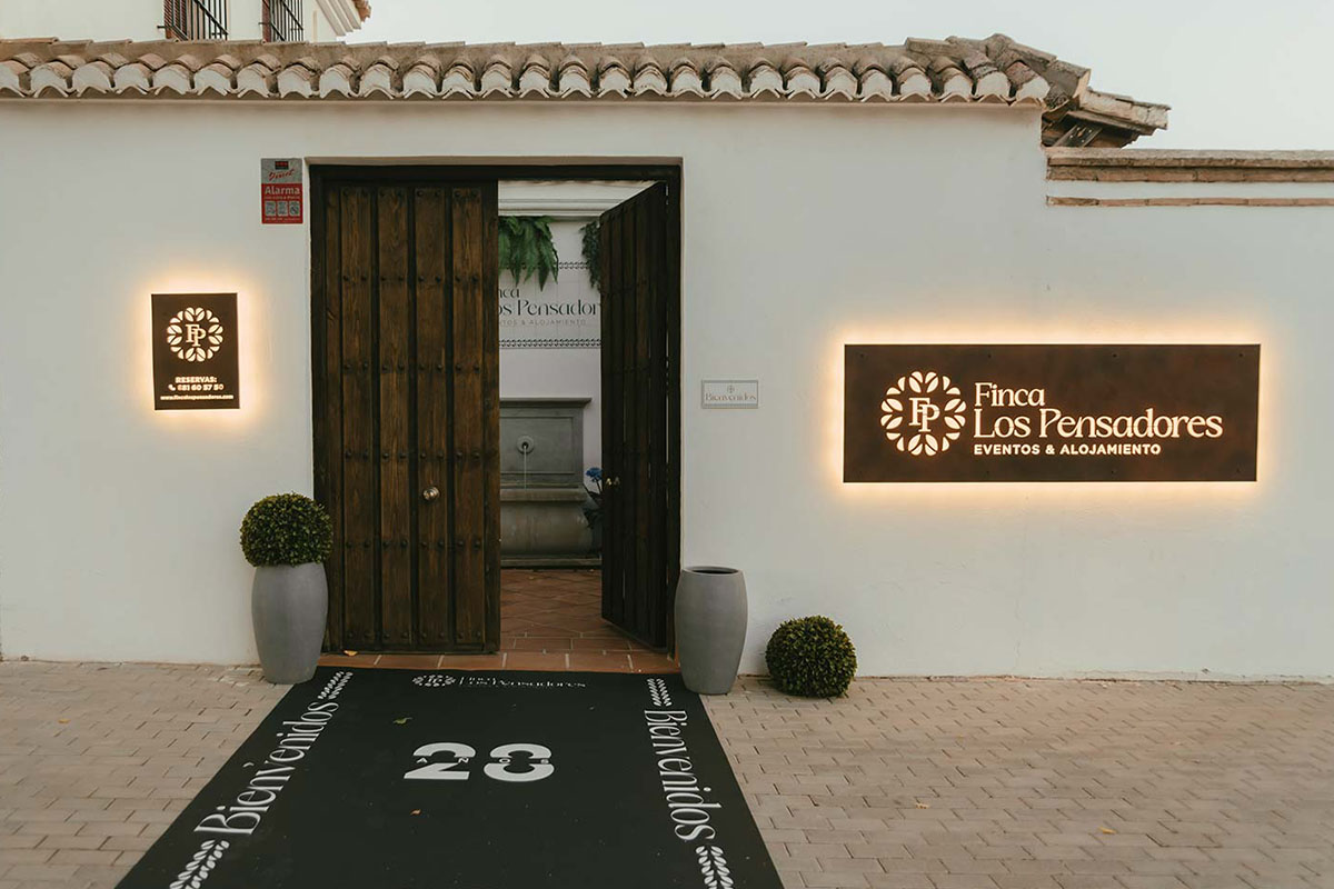 Entrada con letrero luminoso donde se puede leer "Finca Los Pensadores, Eventos y Alojamiento"