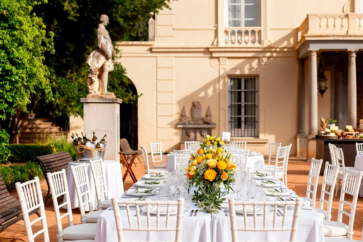 Mesas y sillas para invitados con centros de mesa de flores amarillas preparados para celebración de boda en la explanada del Carmen de los Mártires
