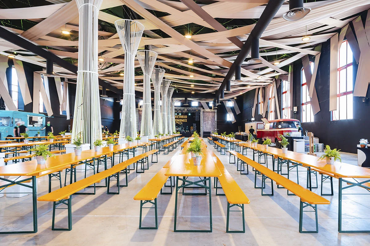 Salón de la azucarera con mesas y sillas largas para albergar una jornada de empresa junto a food trucks en los laterales del salón